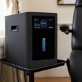 Black air purifier on a stand with a digital display in a room.